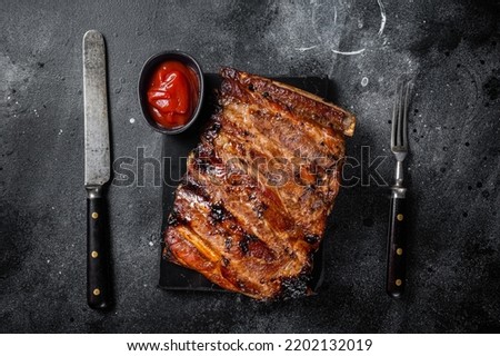 Full rack of BBQ grilled pork spare ribs on a marble board. Black background. Top view. Royalty-Free Stock Photo #2202132019