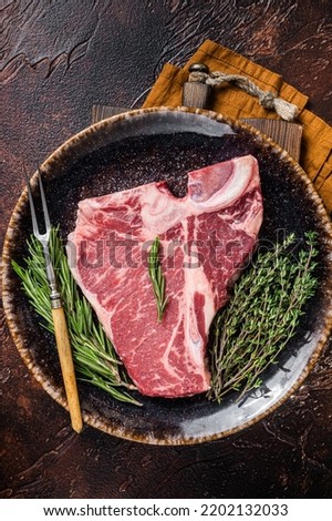 Dry aged Raw porterhouse beef meat Steak, fresh T bone on rustic plate with spices. Dark background. Top view.