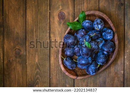 Ripe blue Fresh organic  sweet plums just picked from the tree, walnut wood bowl plate indoors. Autumn Harvest of fruits  rustic  wooden dark black background leaf clay