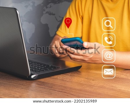 Contact us concept. Woman hand holding smartphone with location red pin symbol and icon search, mail, telephone, and address while sitting at the table. Customer service call center
