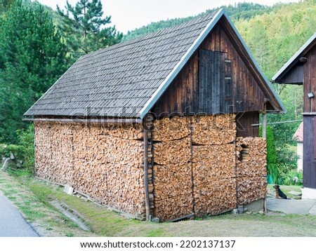 Huge woodshed in the mountains filled with pieces of chopped firewood - airy, with a storage room under a sloping roof on both sides
