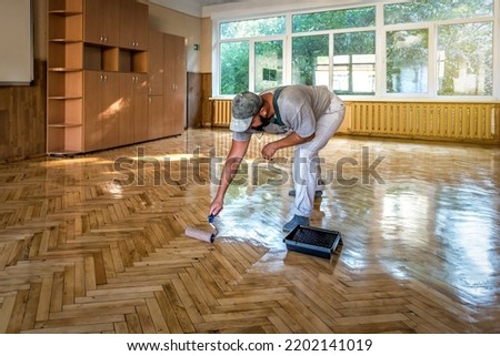 Lacquering parquet floors. Worker uses a roller to coating floors. Varnishing lacquering parquet floor by paint roller - second layer. Home renovation parquet Royalty-Free Stock Photo #2202141019