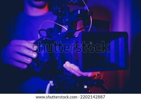 Profession Digital Motion Picture Video Camera in Operators Hands Inside Dark Blue Illuminated Room. TV and Film Production Equipment.