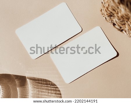 Two blank white cards, basket and glass of water on beige background top view. Forms for business, advertising. Empty space for text. Minimal modern style