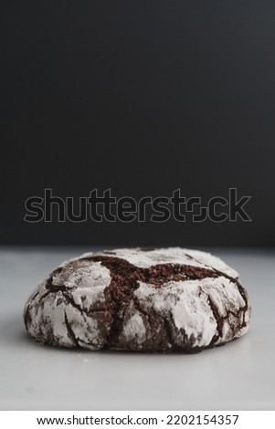 Food photo of freshly baked Chocolate Crinkle Cookies. Close up macro image of a single chocolate iced biscuit. Black and white background with copy space available