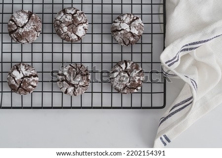 Top down shot food photo of freshly baked Chocolate Crinkle Cookies. Chocolate iced biscuits arranged on black wire cooling rack. White work surface background. Copy space available