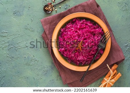 Stewed red cabbage with spices in a clay dish on a green concrete background. Traditional Christmas food. Scandinavian cuisine