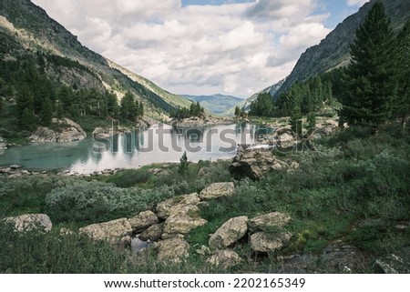 Landscape photography of the lake in the Altai mountains. Turquoise milk water, rocks, stones, reflections, junipers and clouds. Wallpaper, poster, postcard. Calm and peaceful concept. High quality