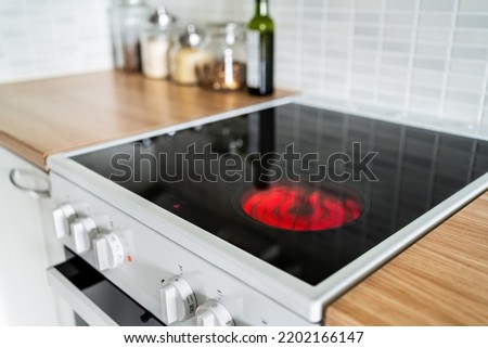 Stove and cooker red hot. Induction, ceramic cooktop, electric stovetop and hob in kitchen. Warm plate ready for cooking. Contemporary interior design, modern counter and wood table. Royalty-Free Stock Photo #2202166147