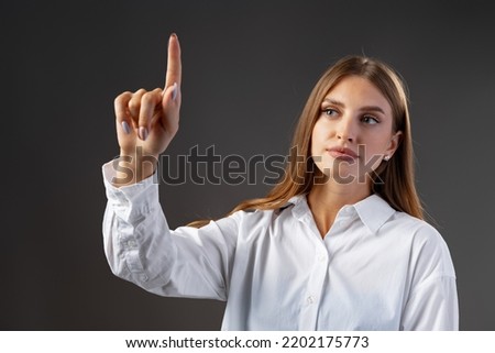 Young female entrepreneur touching virtual screen against grey studio background