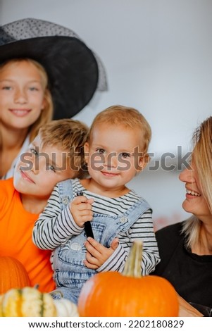 Happy mom with three young kids in halloween costumes are posing on the kitchen among pumpkins decoration. Happiness. Focus is at the baby girl