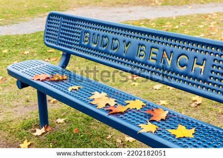 Blue buddy bench in the public park near school in fall Royalty-Free Stock Photo #2202182051