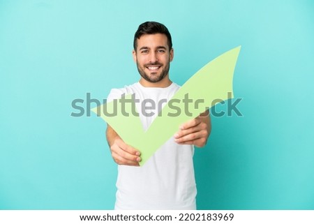 Young handsome caucasian man isolated on blue background holding a check icon with happy expression