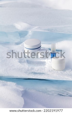Cosmetic products for face and hand skin care in cold winter time. Advertising of nourishing reparative anti-aging cosmetics on podium from natural piece of snowy ice. Empty space for text, mock up 
