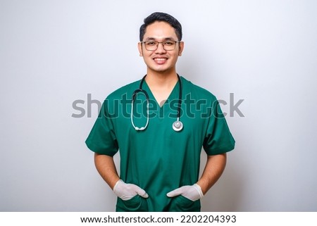 Close-up of professional male doctor or nurse wearing green scrubs, holding hands in pockets and smiling broadly isolated over white background Royalty-Free Stock Photo #2202204393