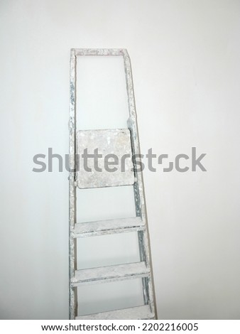 Soiled with paints folding metal ladder-step ladder on background of plastered wall. Concept of repair and finishing works. Copy space. Isolated on white background. Vertical photo.
