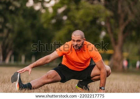 Happy positive sportsman during outdoor workout, man wearing sports outfit warming up muscles,enjoying active lifestyle outside in park. 