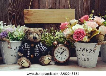 Empty wooden sign hanging with teddy bear and alarm clock on wooden background