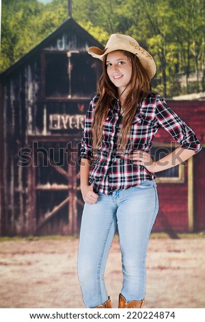 A pretty teen cowgirl standing in front of an old western livery.  