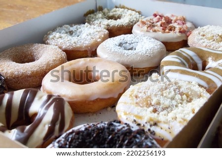 Picture of assorted donuts in a box with chocolate frosted, glazed and Bacon donuts.