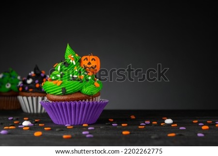 Cupcake on Halloween. Pumpkin Jack o lantern. Dessert on Halloween party. Muffin decorated with colored sprinkles, frosting and Icing shaped pumpkin Jack-o-lantern. Cupcakes on a black wooden table. 