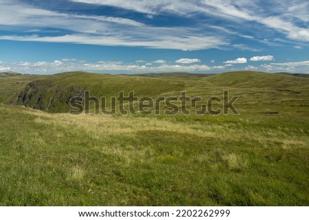 A landscape image looking across a green grassy upland plain to the summit of Tom Buidhe and Tolmount, 2 mountains in the Scottish Highlands. A blue sky is above with white fluffy clouds. Royalty-Free Stock Photo #2202262999