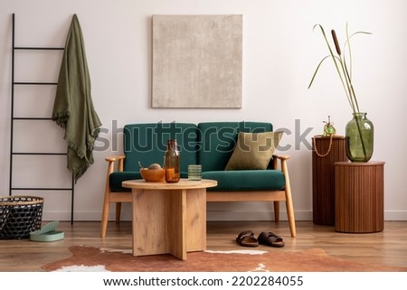 Classic space of living room with mock up poster frame, bottle green sofa, wooden coffee table, ladder, dried flowers in vase and personal accessories. Beige wall. Home decor. Template.	