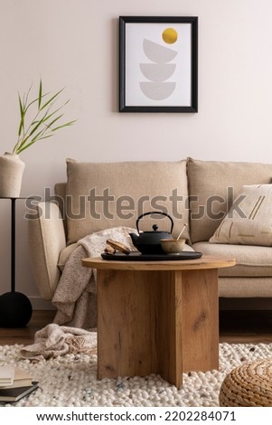 Creative composition of stylish living room with beige sofa, pillow, wooden coffee table, mock up poster frame, black tea pot, side table and elegant decoration. Cozy home decor. Template.	
