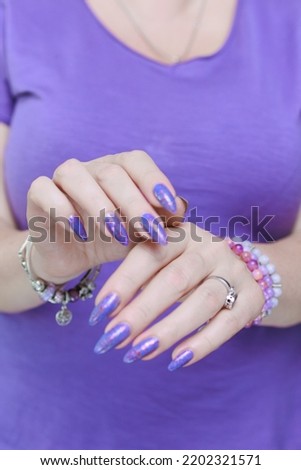 Female hand with long nails and a bottle of lilac purple color nail polish
