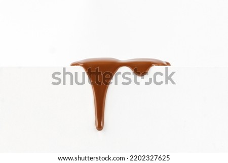 Liquid chocolate sauce dripping. Melted chocolate drop of sweet dark milk chocolate sauce on white pedestal on white background. Royalty-Free Stock Photo #2202327625