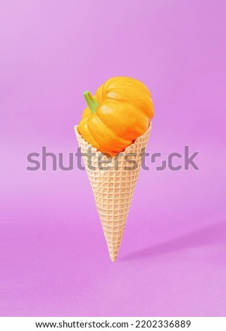 Creative composition with ice cream cone and orange pumpkin against pastel purple background. Tasty autumn sweets concept.
