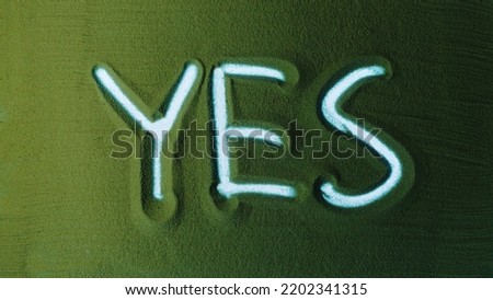 Hand drawing the Word Yes in the Green Sand. Male hand writes the word Yes on the green sand with white backlight. Top view 4k resolution