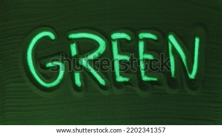 Hand drawing the Word Green in the Green Sand. Male hand writes the word on the sand with green backlight. Top view 4k resolution