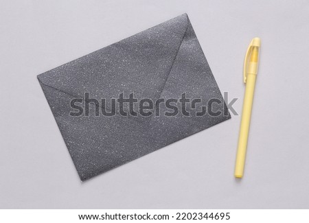 Black envelope with glitter and pen on gray background