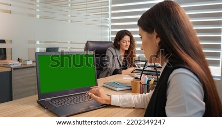 Businessman working on a laptop with green screen on background colleague discussing details. Modern office.