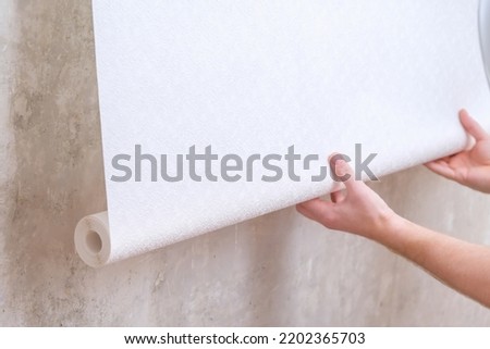 A man rolls out a roll of white wallpaper on the wall with glue. Wallpapering. Repair of a room, apartment, house. Royalty-Free Stock Photo #2202365703