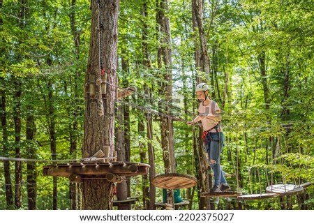 Happy women girl female gliding climbing in extreme road trolley zipline in forest on carabiner safety link on tree to tree top rope adventure park. Family weekend children kids activities concept Royalty-Free Stock Photo #2202375027