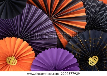 Halloween background from round paper fans. Bright paper fans in purple, orange and black colors of Halloween multi-layered composition. Decorated with two gold glitter pumpkins.