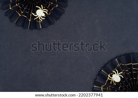 Golden spider and cobweb on a dark background. Scary Halloween shiny spiders and black paper fans with golden cobwebs. Halloween decorations on a black textured backdrop with copy space. Royalty-Free Stock Photo #2202377941