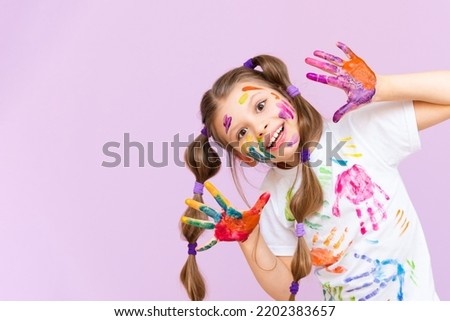 A beautiful little girl stained in multicolored paints on a pink isolated background has fun smiling. Royalty-Free Stock Photo #2202383657