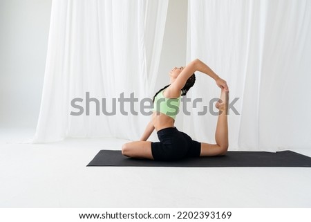 Young flexible brunette girl is doing yoga Eka Pada Rajakapotasana. in a snow-white room