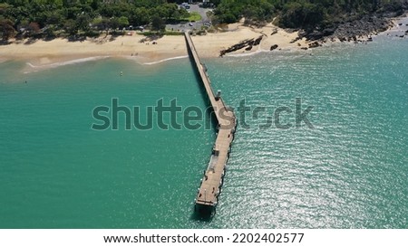 A pier on an Australian beach surrounded by green mountains