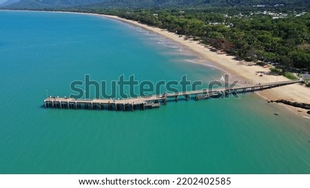 A pier on an Australian beach surrounded by green mountains