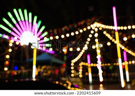 Blurry rollercoaster in bokeh, Ferris wheel at night of colorful with outdoor, Defocused (blurred) and blur image of Amusement park, The annual temple event has activities. Image out of focus Royalty-Free Stock Photo #2202415609