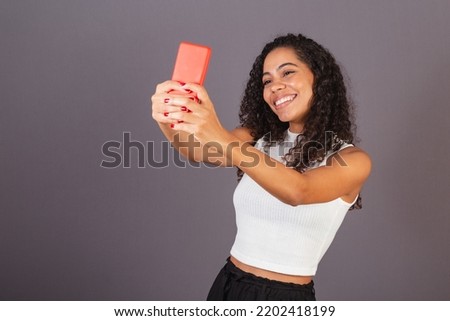 Young Brazilian black woman taking selfie, self portrait with red cellphone.