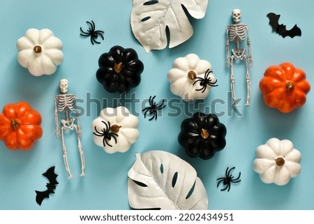 Halloween holiday composition with decorations of pumpkins, bats, spiders, leaves and skeletons on light blue background. Happy halloween greeting card. Top view with copy space. Flat lay.