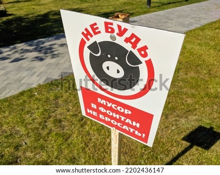 Close-up of a sign on a green lawn. Translation: Don't be a pig. Don't throw trash into the fountain.