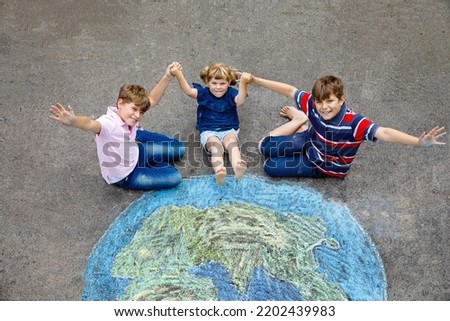 Little preschool girl and two school kids boys with earth globe painting with colorful chalks on ground. Happy earth day concept. Creation of children for saving world, environment and ecology.