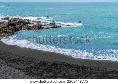 Playa Chica beach with black sand in Puerto de la Cruz in the Canary Islands, Spain. Atlantic Ocean coastline and rocks in blue raging water with white foam whipped up by waves