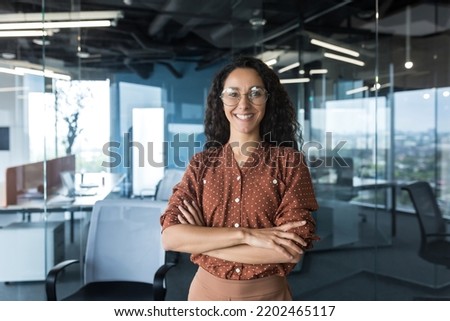 Young successful Indian IT developer female engineer working inside the office of a development company portrait of a female programmer with curly hair and glasses, smiling and looking at the camera. Royalty-Free Stock Photo #2202465117